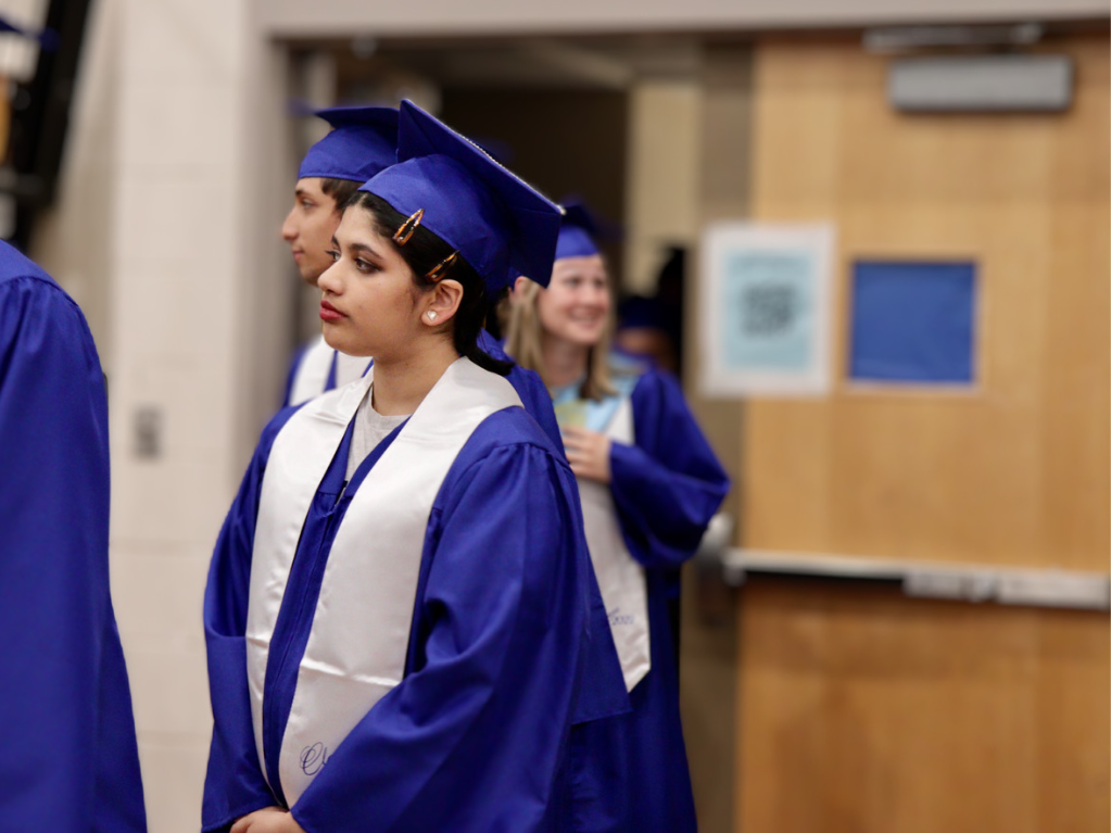 A student wearing a blue cap and gown lines up with classmates during Class Day